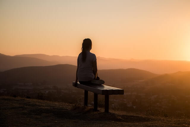 Woman sitting on a bench watching a sunset.